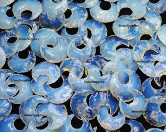 May include: A collection of translucent blue and white opalite crescent moon shaped stones. The stones are smooth and polished, with a variety of sizes and shapes. The stones are arranged in a random pattern, with some overlapping. The text "StoneSupplier" appears multiple times in the image.