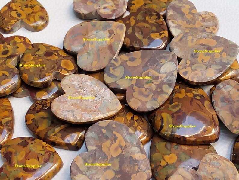 May include: A collection of heart-shaped polished stones with a brown, yellow, and green marbled pattern. The stones are arranged in a pile and have a glossy finish.  StoneSupplier is printed on several of the stones.