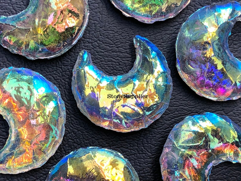 May include: A collection of iridescent glass crescent moon shapes. The glass is clear with a rainbow sheen. The moons are various sizes and are arranged on a black surface.  StoneSupplier is printed on one of the moons.