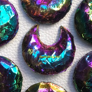 May include: A group of iridescent rainbow moonstone crescent shapes. The stones are polished and have a smooth, shiny surface. The stones are arranged in a semi-circle on a white background.