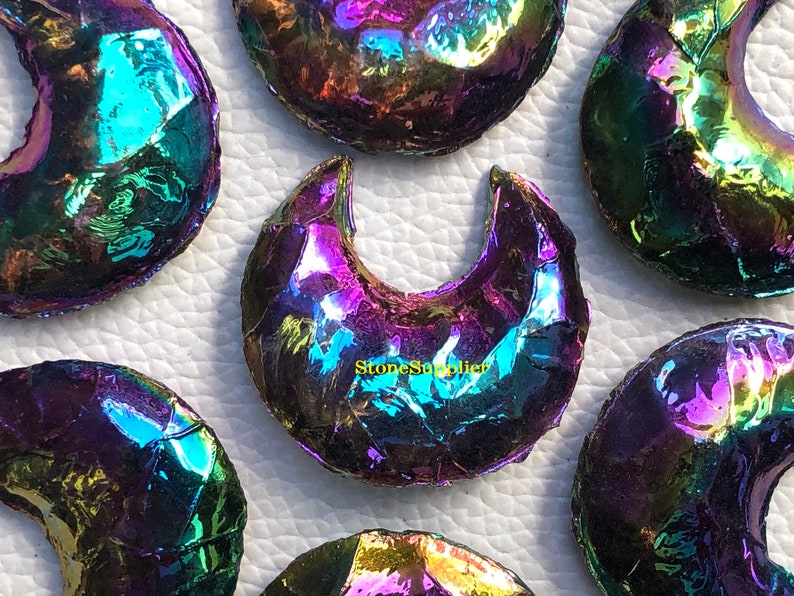 May include: A group of iridescent rainbow moonstone crescent shapes. The stones are polished and have a smooth, shiny surface. The stones are arranged in a semi-circle on a white background.