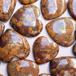 May include: A collection of 10 heart-shaped, polished, brown and gold jasper cabochons. The cabochons have a mottled, marbled pattern with a high gloss finish.