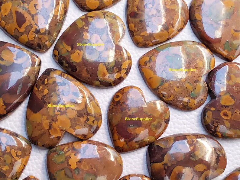 May include: A collection of 10 heart-shaped, polished, brown and gold jasper cabochons. The cabochons have a mottled, marbled pattern with a high gloss finish.
