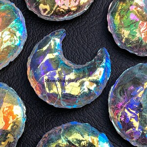 May include: A collection of iridescent glass crescent moon shapes. The glass is clear with a rainbow sheen.