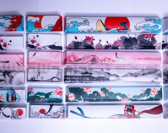May include: A set of 10 colorful keyboard keycaps with Japanese-inspired designs. The keycaps feature images of waves, flowers, and traditional architecture. The keycaps are numbered 1 through 10.