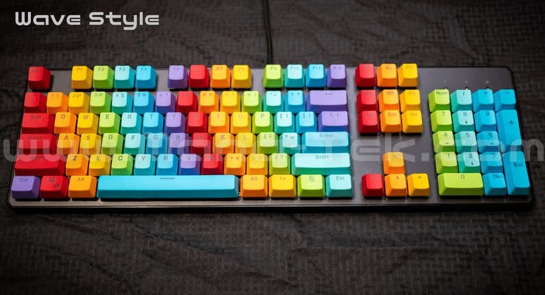 May include: A full-sized keyboard with rainbow-colored keycaps. The keys are arranged in a standard QWERTY layout, with each row of keys displaying a different color. The keyboard has a black frame and a black cable.