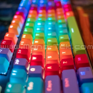 May include: Close-up of a backlit mechanical keyboard with rainbow-colored keycaps. The keys are arranged in rows, with each key displaying a different color, including red, orange, yellow, green, blue, and purple. The keyboard has the text "www.mang-tek.com" on the side.