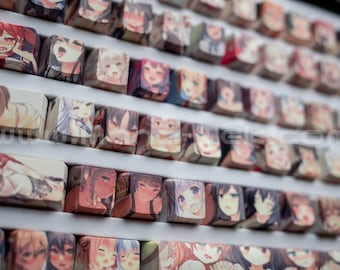 May include: A close-up of a keyboard with custom keycaps featuring anime-style illustrations of female characters. The keycaps are arranged in rows and columns, creating a colorful and visually appealing pattern.