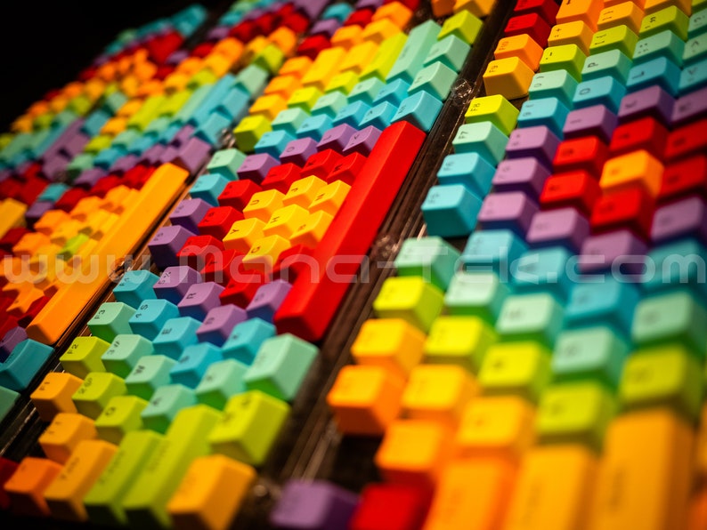 May include: A vibrant display of colorful keyboard keys arranged in rows. The keys are a spectrum of colors, including red, orange, yellow, green, blue, and purple. The image has a shallow depth of field, focusing on the keys.