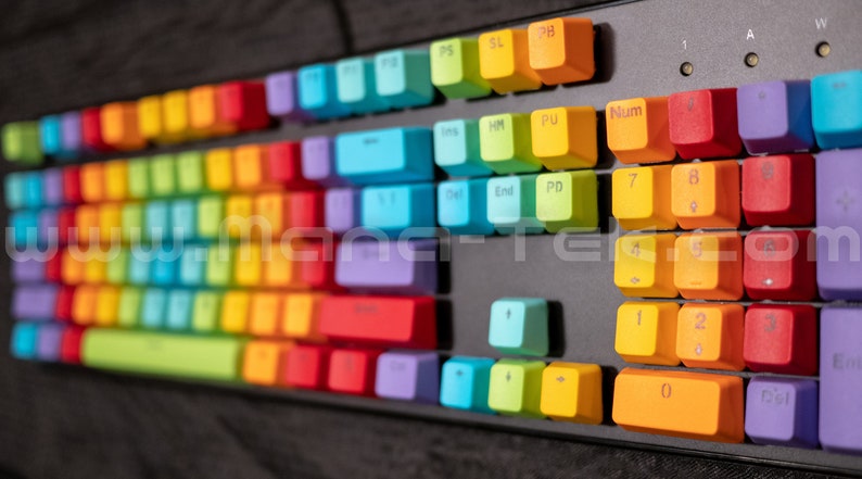 May include: A mechanical keyboard with rainbow-colored keycaps. The keys are arranged in a standard layout, with each row featuring a different color. The keycaps have various symbols and letters printed on them. The keyboard is on a dark surface.