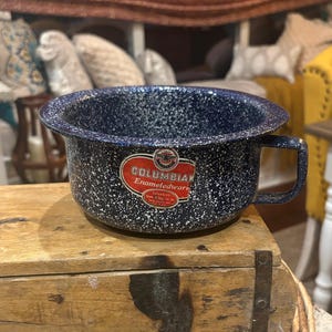 May include: A blue and white speckled enamelware bowl with a handle. The bowl has a dark blue base with white speckles. A red and white label reads "COLUMBIAN Enameledware".