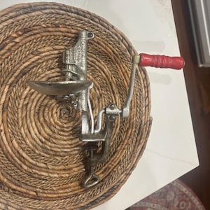 May include: A vintage metal reloading tool with a red wooden handle. The tool is silver and has a clamp to attach to a surface. The handle is red. The tool is designed for reloading ammunition.