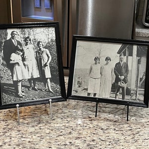 May include: Two black framed photographs of families from the early 1900s. The photos are displayed on small black easel stands.