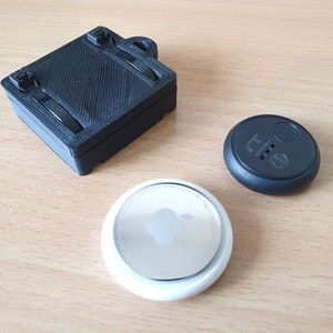 Op de afbeelding: Een zwarte Tile Mate Bluetooth-tracker, een zwarte Tile Slim Bluetooth-tracker en een zilveren batterij voor een Tile-tracker.