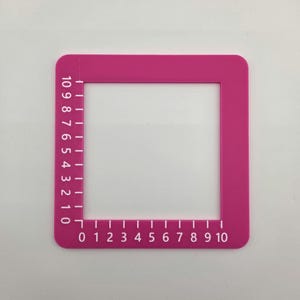 Könnte beinhalten: Ein quadratischer Messrahmen aus rosa Kunststoff mit weiß aufgedruckten Markierungen. Die linke Seite verfügt über eine vertikale Skala von 0 bis 10 und die Unterkante über eine horizontale Skala von 0 bis 10 zur präzisen Messung von Objekten.
