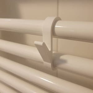 Puede incluir: Gancho de plástico blanco diseñado para colgar objetos en un radiador blanco.