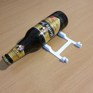 Puede incluir: Un soporte para botellas de plástico blanco con una botella de cerveza de vidrio marrón descansando encima. La etiqueta de la botella dice "Naturtrübe Bier" y "Traditionelle Braukunst".