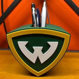 May include: A green and yellow shield-shaped desk organizer with a white "W" in the center. Three pens are in the organizer.