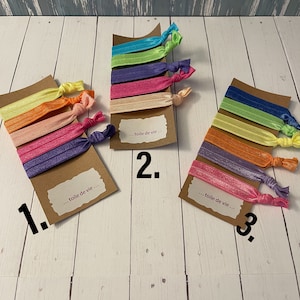 May include: Three sets of colorful elastic hair ties on brown card stock with the text "...toile de vie..." and numbers 1, 2, and 3.