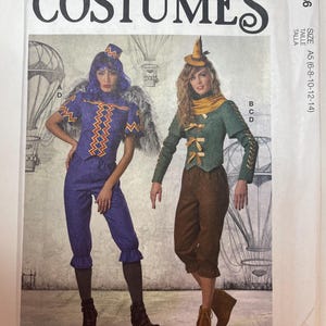 May include: A McCall's M8186 sewing pattern envelope for costumes in sizes A5 (6-8-10-12-14). The front shows two outfits: one with a purple top and pants with orange zigzag trim and a small hat, and another with a green jacket, brown pants, and a pointed hat.