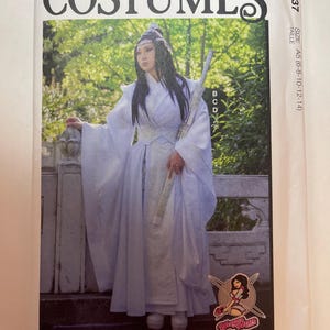 May include: A McCall's Costumes sewing pattern envelope M8337, size A5 (6-8-10-12-14). The front features a photograph of a person wearing a white, layered, long-sleeved robe with wide sleeves, a high collar, and a wide waist sash, holding a long sword.