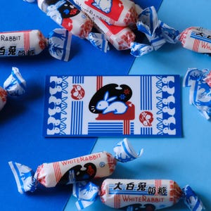 May include: Assortment of White Rabbit candy wrappers with blue and white stripes and a white rabbit logo. The wrappers feature the text "White Rabbit" and "大白兔奶糖" in Chinese characters.