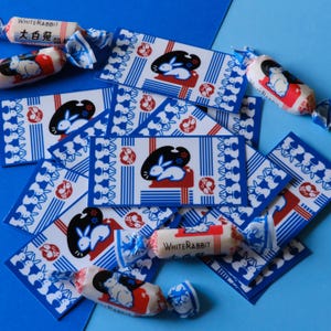 May include: A stack of blue and white patterned cards with a white rabbit design. The cards are surrounded by white rabbit candy wrappers with the text "White Rabbit" and "大白兔奶糖" printed on them.