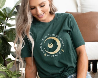 May include: A dark green t-shirt with a gold crescent moon and the text "there is magic in all of us".