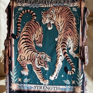 May include: A tapestry featuring two tigers with a green background. The tapestry has a border with gold and white accents. The text "VIII STRENGTH" is printed at the bottom of the tapestry.
