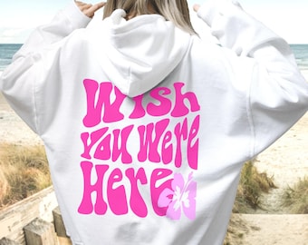 Puede incluir: Sudadera con capucha blanca con un gráfico rosa "Wish You Were Here" y una flor rosa en la espalda.