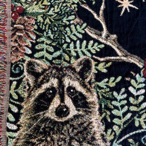 Raccoon Christmas Holiday blanket. The perfect raccoon Christmas gift for raccoon lovers, this raccoon woven tapestry blanket has six detailed raccoons woven into a black background. The raccoons are surrounded by winter botanicals and red bows.