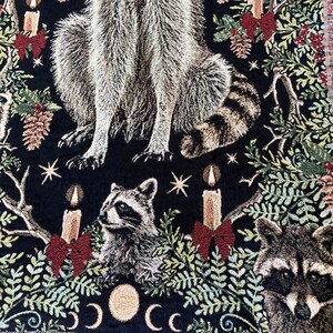 Raccoon woven tapestry blanket. All cotton with a black background a large raccoon sits in the center of botanicals, christmas candles, red bows, pinecones, holly berries and several other cheeky raccoons. Adorable christmas gift for raccoon lovers.
