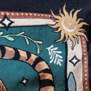 May include: A tapestry with a teal background featuring a tiger, a sun, and a stylized tree. The tiger is brown and black with orange stripes. The sun is yellow with a white face. The tree is white with green leaves.