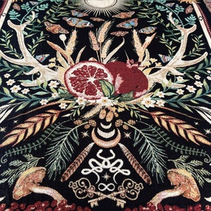 May include: A black tapestry with a detailed design of antlers, pomegranates, and a crescent moon. The tapestry features a variety of floral elements, including leaves, flowers, and wheat stalks. The tapestry is woven with gold, red, and green threads.