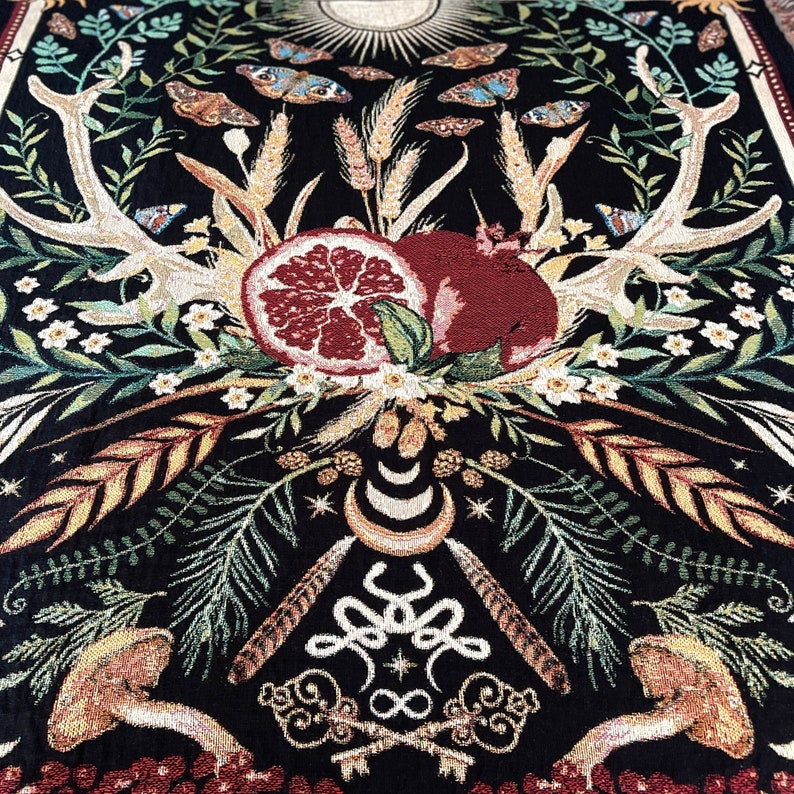 May include: A black tapestry with a detailed design of antlers, pomegranates, and a crescent moon. The tapestry features a variety of floral elements, including leaves, flowers, and wheat stalks. The tapestry is woven with gold, red, and green threads.