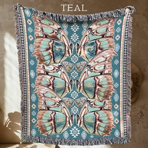 May include: Teal-colored woven throw blanket featuring a butterfly wing design. The blanket has a fringe border and a geometric pattern along the edges. The word "TEAL" is printed at the top. The butterfly wings are in shades of teal, brown, and cream.