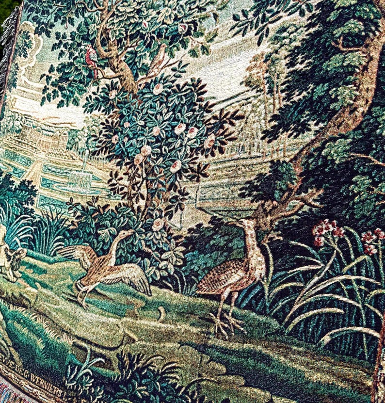 May include: A woven tapestry featuring a landscape scene with two birds in the foreground, one with wings spread and one standing. The background displays lush green trees, flowering bushes, and a distant architectural structure with a fountain.