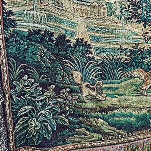 May include: A woven tapestry featuring a garden scene with fountains, lush green foliage, a small dog, and a bird. The lower right corner displays the text LAVEVVE DE G WERNIERS. The fabric has a textured, multi-colored thread construction.