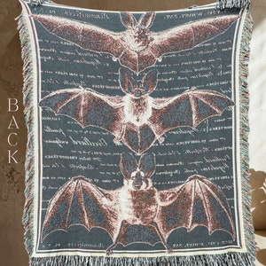 May include: A woven tapestry featuring three detailed illustrations of bats on a dark blue background. The bats are depicted in a vintage style with intricate details and are surrounded by text in a script font.