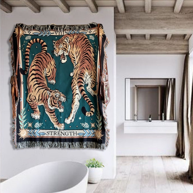 May include: A tapestry wall hanging with a green background featuring two tigers. The tigers are facing each other, one is standing on its hind legs and the other is lying down. The tapestry has a fringe border and the text "STRENGTH" is printed at the bottom.