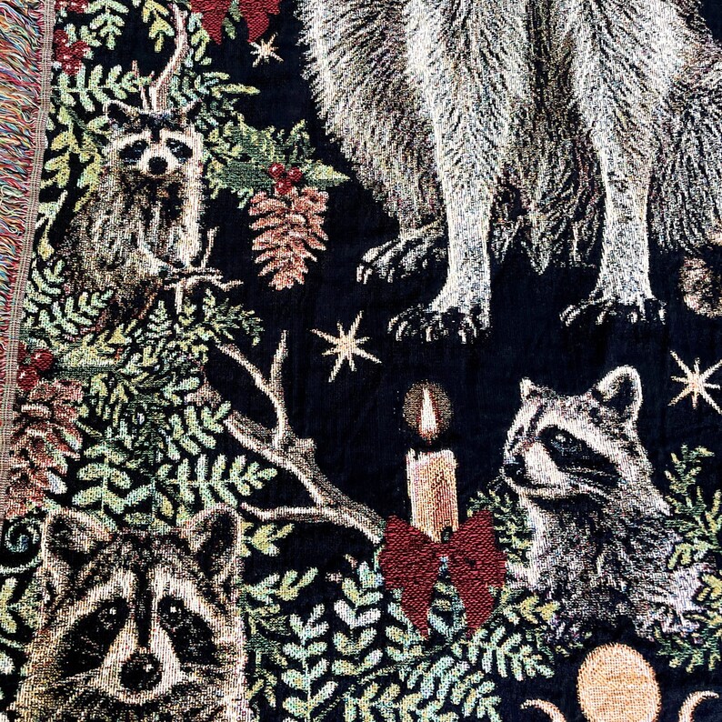The ideal hygge gift for raccoon lovers, this raccoon blanket is adorable. Several cute raccoons are woven into a black background surrounded by greenery, mistletoe, holly berries, pine cones, Christmas candles and red bows.