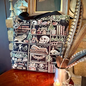 With a vintage Halloween aesthetic, this HERBAL APOTHECARY WOVEN TAPESTRY TOTE BAG has a witchy book nook aesthetic that will delight dark academia, vulture culture, oddities & whimsigoth lovers alike. Highly detailed apothecary bottles, mushrooms, stars, owls, skulls, hanging herbs, feather quills, snakes, crystals, a drunken mandrake with his bubbling tankard & more are expertly woven into every inch of this special woven tapestry tote bag.