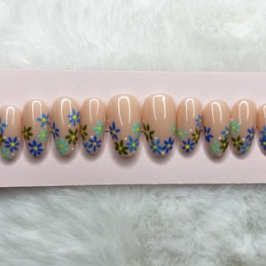 Peut inclure: Un ensemble de dix faux ongles ovales avec une base rose clair et un motif floral. Les fleurs sont bleues, vertes et blanches.