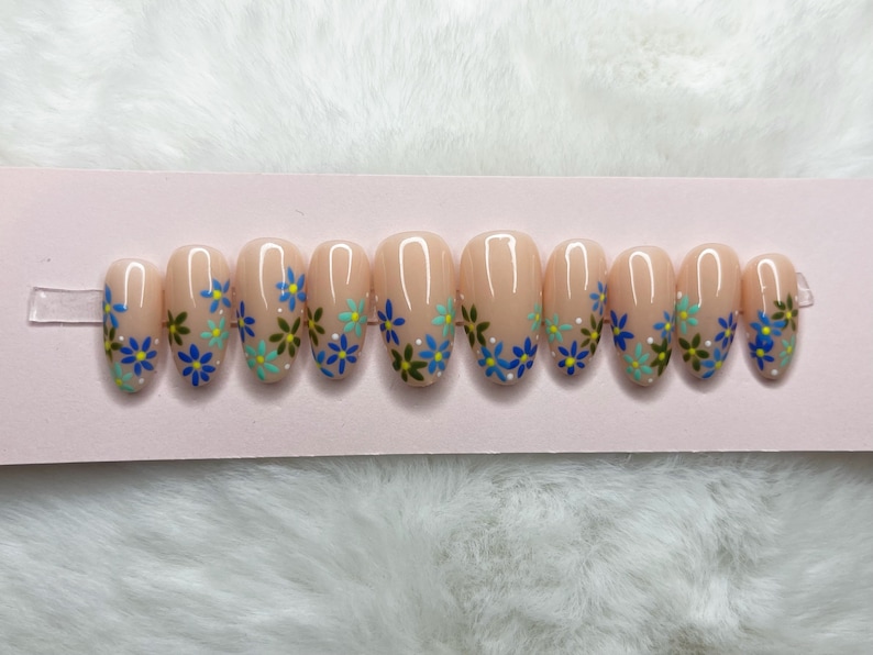 Peut inclure: Un ensemble de dix faux ongles ovales avec une base rose clair et un motif floral. Les fleurs sont bleues, vertes et blanches.