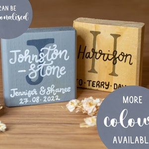 Könnte beinhalten: Zwei Holzblöcke mit personalisierten Namen und Daten. Der Block links ist grau und sagt "Johnston - Stone Jennifer & Shanee 27.08.2022". Der Block rechts ist hellbraun und sagt "Harrison O-Terry. Da".