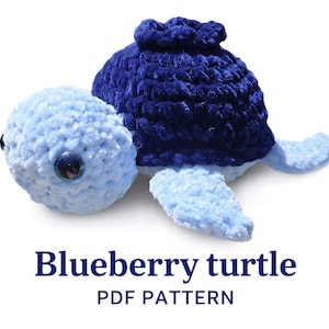 May include: A crocheted turtle toy with a light blue head and flippers, a dark blue shell, and black plastic eyes. Below the turtle, the text reads: Blueberry turtle PDF PATTERN. The toy is made of soft, textured yarn with a plush appearance.