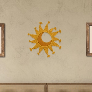 May include: A yellow macrame sun wall hanging with a crescent moon shape in the center. The sun is hanging on a beige wall above a bed with a woven headboard and beige bedding.