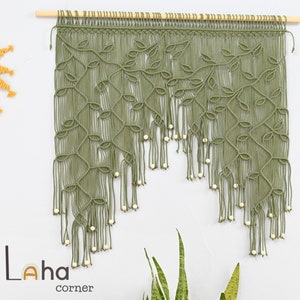 May include: A green macrame wall hanging with a leaf design and white beads. The hanging is attached to a wooden dowel rod.