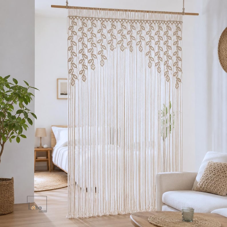 May include: A cream-colored macrame room divider hanging from a wooden rod. The top section features a repeating pattern of knotted leaf shapes, while the lower portion consists of long, vertical, unknotted fringe strands that hang straight down.