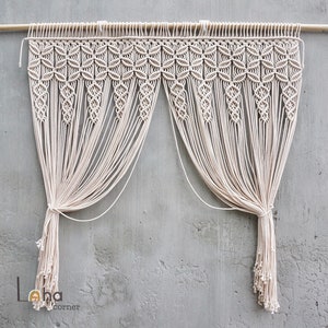 May include: A white macrame wall hanging with a decorative pattern at the top and long tassels at the bottom. The hanging is made of natural cotton cord and is a popular bohemian decor item.
